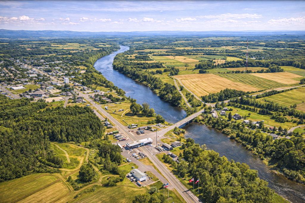 Aerial view of the Canadian border near Caribou, Maine, showing the Aroostook River, farmland, forest, and international border crossing between the United States and New Brunswick on a bright summer day.